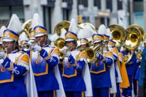 Members of the Alcorn State University Sounds of Dyn-O-Mite marching band in blue and gold uniforms play brass instruments while marching in the 2025 Macy’s Thanksgiving Day Parade in New York City.